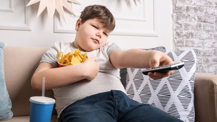 Overweight boy eating chips and sitting on couch.